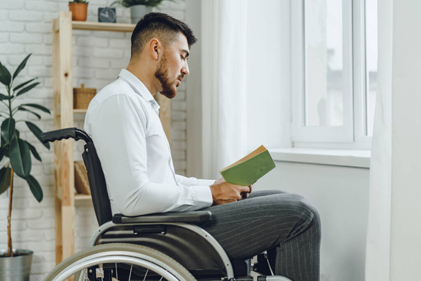 Людина з обмеженими можливостями в інвалідному візку читає книгу в приміщенні
 - Фото, зображення