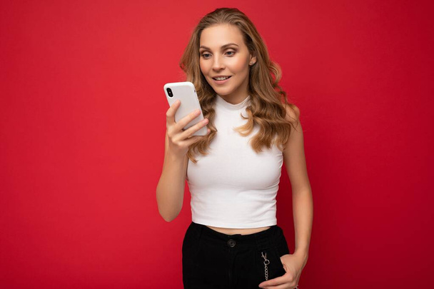 Fotoshooting von attraktiven positiv gut aussehende junge Frau trägt lässig stilvolles Outfit posiert isoliert auf dem Hintergrund mit leeren Raum halten in der Hand und mit Handy-Nachrichten-SMS Blick auf - Foto, Bild