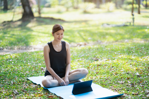 Young woman learning yoga exercise on a video conference outdoor in the park, sport yoga concept - Фото, зображення