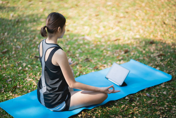 Genç bir kadın parkta bir video konferansında yoga egzersizi öğreniyor. Spor yoga konsepti. - Fotoğraf, Görsel