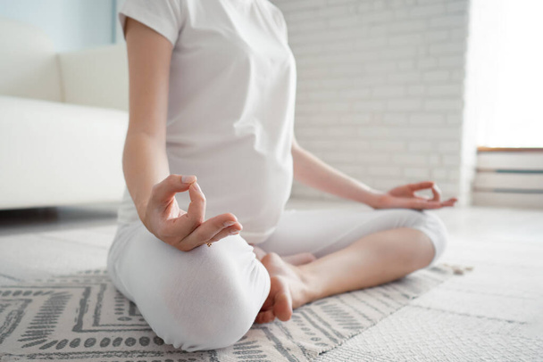 穏やかな妊娠中の女性瞑想で座っている蓮の位置で床にラグとともに自宅 - 写真・画像