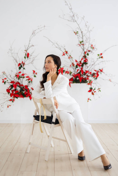 Portrait of young caucasian brunette woman posing on chair in a stylish and elegant pantsuit. Evening equipment, outfit for the celebration. Wedding suit with trousers, modern style. - Foto, imagen