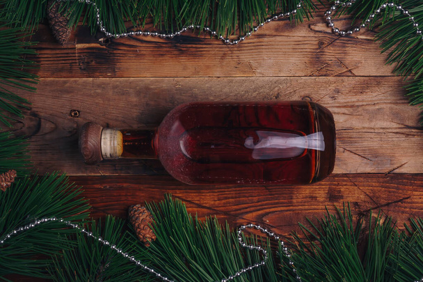 メリークリスマスの木製の背景にコニャックのボトル、コーンやビーズでフレーム新鮮な松の木の枝。トップビュー、垂直ショット。お祝いのお酒 - 写真・画像