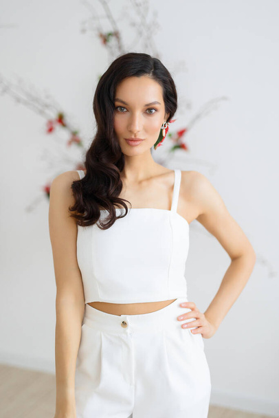 A young caucasian brunette woman in a stylish and elegant pantsuit holding a jacket. Bride posing against the background of an unusual composition of fresh flowers poinsetia for an chamber wedding ceremony - Photo, Image