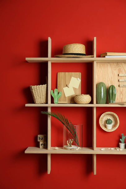 Stylish wooden shelves with decorative elements on red wall - Fotoğraf, Görsel