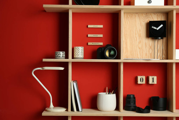 Stylish wooden shelves with photography equipment and decorative elements on red wall - Fotografie, Obrázek