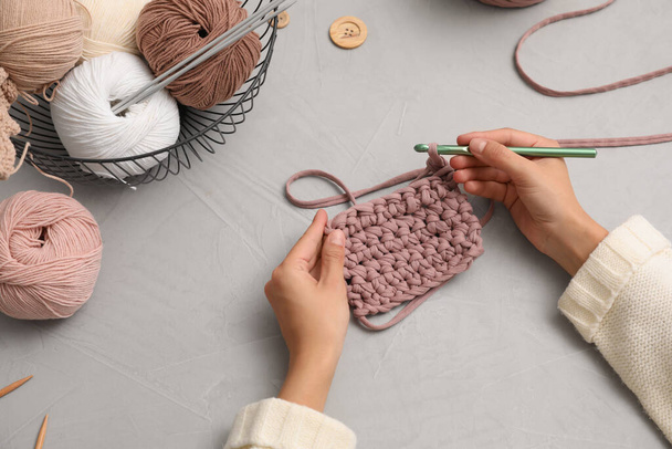 Woman crocheting with threads at grey table, closeup. Engaging hobby - Фото, зображення