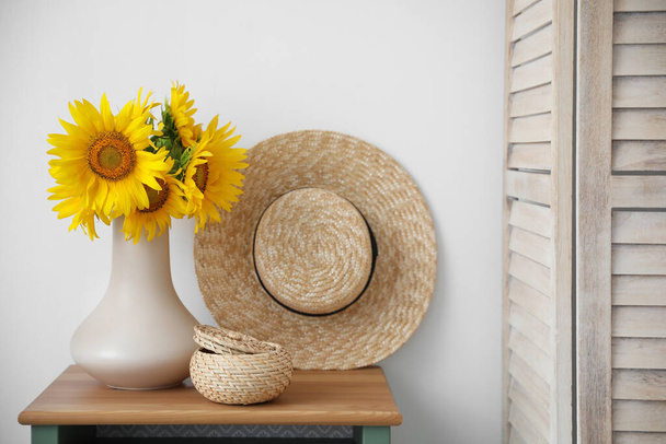Bouquet of beautiful sunflowers, wicker basket and hat on table indoors - Photo, image