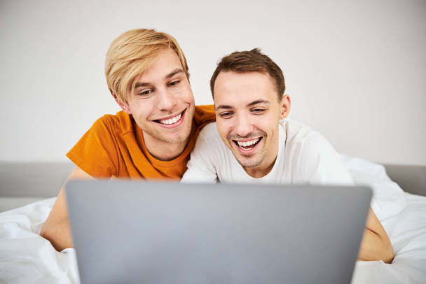 Happy homosexual couple watching movie together on laptop - Zdjęcie, obraz