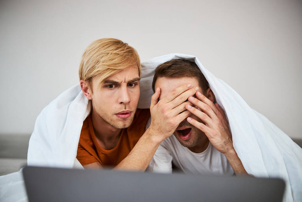 Beautiful homosexual couple watching scary movie on notebook - Photo, Image
