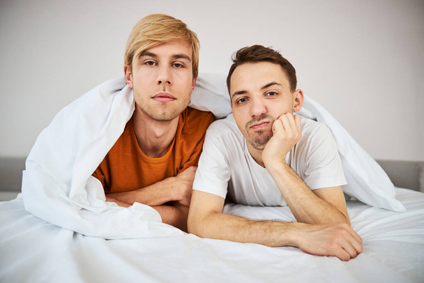 Χαριτωμένο ομοφυλόφιλο ζευγάρι ξαπλωμένο στο κρεβάτι στο σπίτι - Φωτογραφία, εικόνα