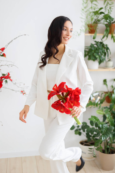 Fashionable bride in a white trouser suit. Ceremony arch of red poinsettia. Wedding in winter season. - Fotoğraf, Görsel