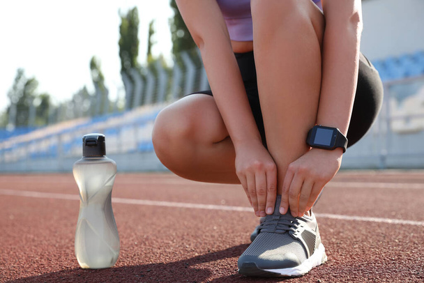 Woman with fitness tracker tying shoelaces at stadium, closeup - Photo, Image