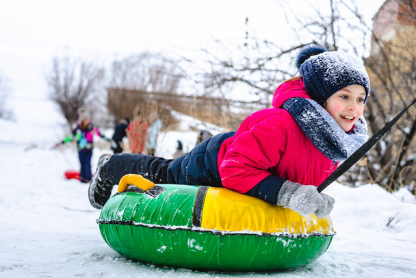 Glückliches kleines Mädchen rutscht auf einer Röhre eine Rutsche im Schnee hinunter und macht Winterspaß - Foto, Bild
