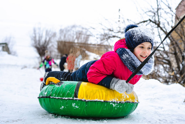 Feliz niña se desliza por un tobogán en la nieve en un tubo, tubo de diversión de invierno - Foto, Imagen