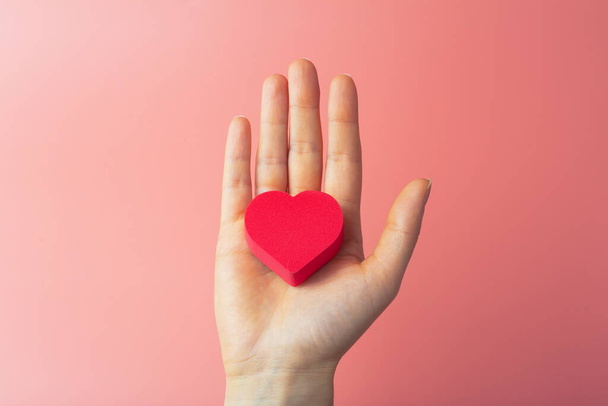 Heart in the hands of a female on a colored background. Donation, charity, health treatment, help concept. Background for Valentine's Day (February 14) and love. - Photo, Image