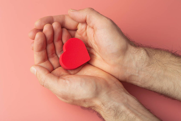 Corazón en las manos de un hombre sobre un fondo de color. Donación, caridad, tratamiento de salud, concepto de ayuda. Fondo para el Día de San Valentín (14 de febrero) y el amor. - Foto, Imagen