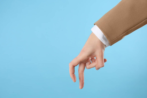 Businesswoman imitating walk with hand on light blue background, closeup. Finger gesture - 写真・画像