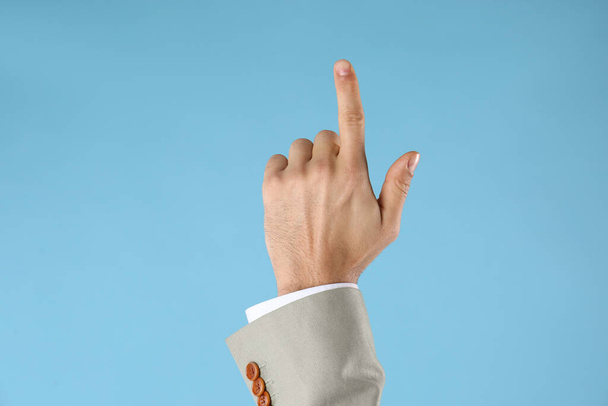 Businessman pointing at something on light blue background, closeup. Finger gesture - Fotoğraf, Görsel