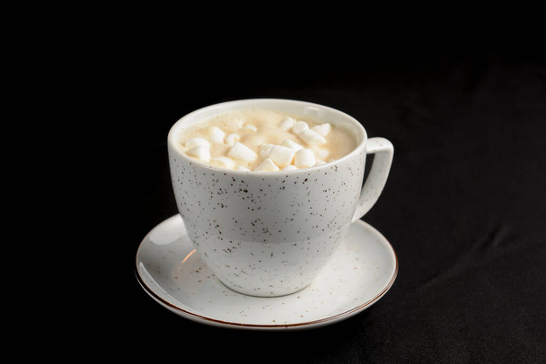 Cup of caramel latte coffee with marshmallows on black background. Delicious sweet sugar coffee in a white cup. - Foto, afbeelding