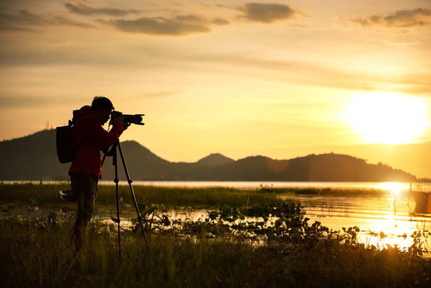 Cestovní fotograf s přírodou jezera při západu slunce s kamerou na stativ. - Fotografie, Obrázek