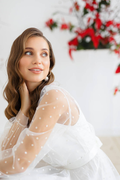 Wedding Dress Trends and Fashion. Fashionable bride in a white wedding dress posing against the background of an unusual composition of fresh flowers poinsetia for an chamber wedding ceremony - Foto, afbeelding