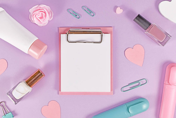 Clipboard with empty paper for text surrounded by hearts, beauty producs and stationery items on pastel violet background - Foto, Imagem