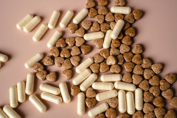 White capsules and beige pills on a pink background. - Photo, Image