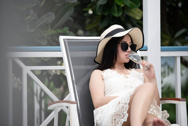Mujer joven sentada bebiendo agua mientras está relajada tumbada en una tumbona en el hotel. - Foto, imagen