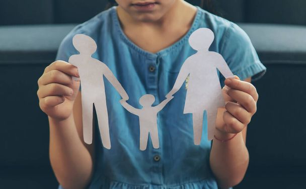 Egy gyerek egy papírcsaláddal a kezében. a válás, a felügyeleti jog és a gyermekbántalmazás fogalma. Szelektív fókusz. Emberek.. - Fotó, kép