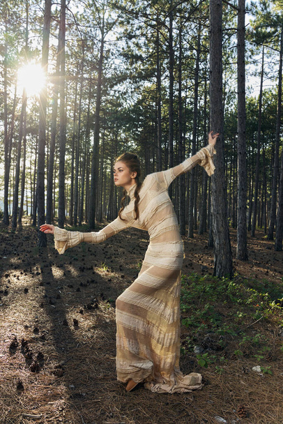 A romantic woman in a dress in a coniferous forest is dancing on the ground and fallen cones - 写真・画像