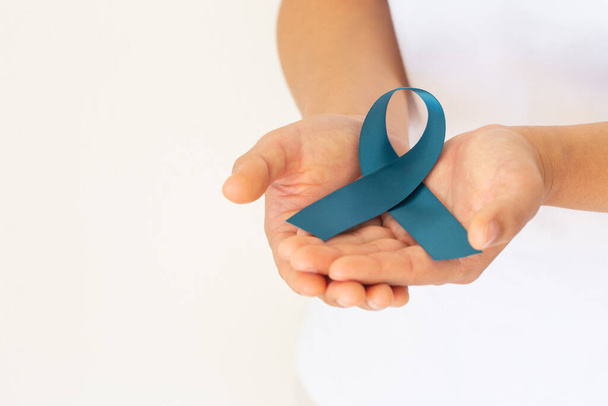 Hand holding teal color ribbon on white background with copy space. Ovarian Cancer Awareness, Gynecological, Uterine Cancer, Vulvar Cancer, Panic Disorder, Post Traumatic Stress Disorder (PTSD). - Fotografie, Obrázek