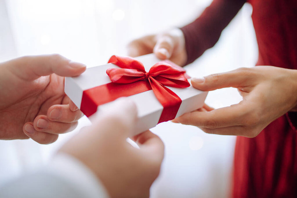 Valentine's day concept. A giftbox with red ribbon in hands. Loving couple give each other presents on 14 February. Romantic Boyfriend and girlfriend celebrating lover's day - Fotó, kép