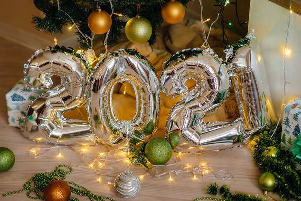 Happy New Year 2021. Festive silver metal balloons with numbers 2021 on the background of light bulbs and garlands decorated with a Christmas tree - Fotó, kép