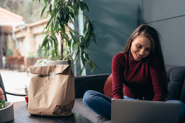 take away food in paper bag, woman using laptop in background - Fotó, kép