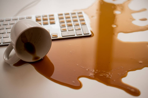 Spilled black coffee on a computer keyboard at a white table - Photo, Image