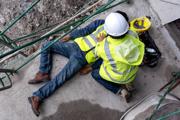 Erste-Hilfe-Unfall eines Bauarbeiters vor Ort. Bauarbeiter stürzt bei Unfall auf Baugerüst, Sicherheitsteam hilft Mitarbeitern bei Unfall. - Foto, Bild