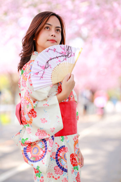 Portrait d'un voyageur jeune femme asiatique porter une robe yukata et marcher sur le chemin de l'arbre dans le parc japonais de sakura en fleurs de cerisier à la lumière du soleil après-midi. - Photo, image