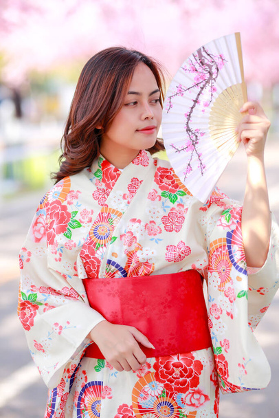 旅行者の肖像若いアジア人女性が浴衣を着て日差しの日の午後に桜公園を開花日本の木の道を歩く. - 写真・画像