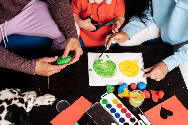 mom, dad, son and their dog play with plasticine and paint at home - Photo, Image