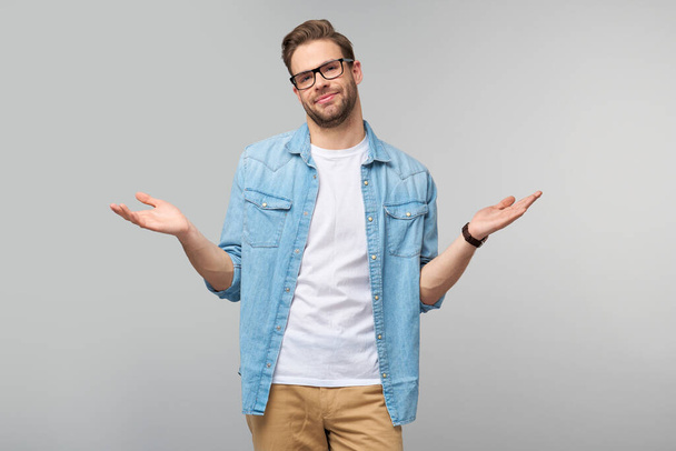 Portrait of confused clueless young man in jeans shirt standing over grey background - Photo, Image