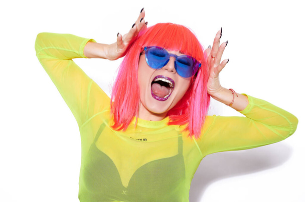 Chica gritando en peluca rosa, gafas de sol azul de moda, y con labios brillantes sobre fondo blanco - Foto, Imagen