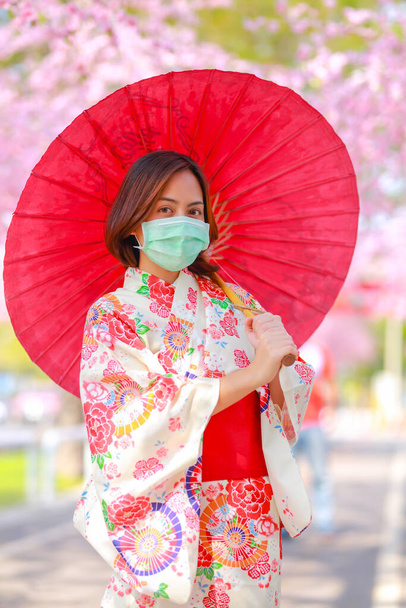 旅行者の若いアジアの女性の肖像は、ドレス浴衣を着て、コロナウイルス(COVID-19)から保護するために外科用マスクを着用しています。概念観光客はコロナウイルスの流行後にアジアを旅します. - 写真・画像