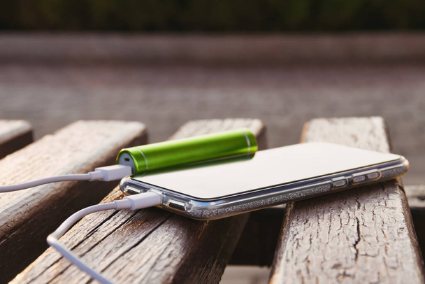 Smartphone and external power bank lie on a wooden bench in the park while charging. - Zdjęcie, obraz