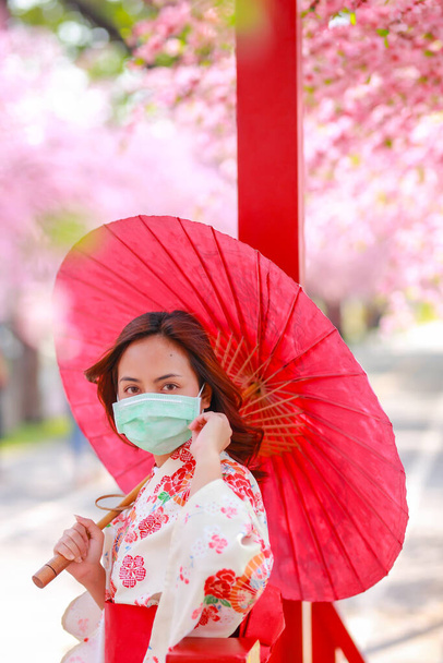 Portrét cestovatele mladé asijské ženy nosit šaty Yukata a nosit chirurgickou masku na ochranu před Coronavirem (COVID-19). koncept turisté cestovat v Asii po epidemii koronaviru. - Fotografie, Obrázek