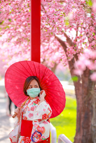 Retrato de una joven mujer asiática viajera que usa un vestido yukata y una máscara quirúrgica para protegerse del Coronavirus (COVID-19). concepto turistas viajan en Asia después de la epidemia de coronavirus. - Foto, Imagen