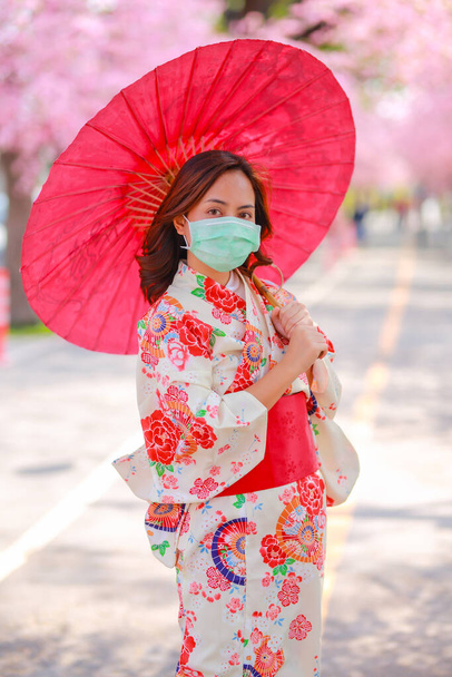 Egy utazó fiatal ázsiai nő portréja Yukata ruhát visel, és sebészeti maszkot visel, hogy megvédje a Coronavirustól (COVID-19). koncepció turisták utazás Ázsiában után a koronavírus járvány. - Fotó, kép