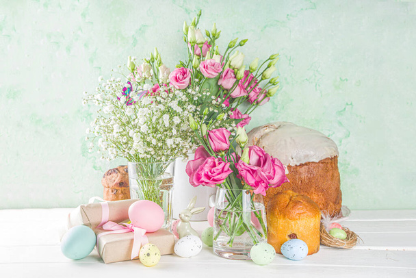ハッピーイースターの挨拶、招待状の背景。青い木製のテーブルの上にカラフルなイースターエッグと春の花と春の花の組成物、テキスト用のコピースペース。フラットレイアウト、トップビュー. - 写真・画像