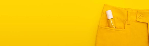 πάνω όψη γυάλινη φιάλη με βερνίκι νυχιών στην τσέπη του παντελόνι που απομονώνονται σε κίτρινο, banner - Φωτογραφία, εικόνα