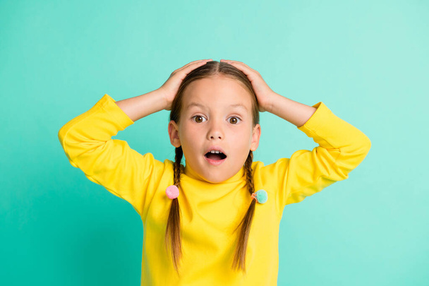 Photo of astonished surprised little schoolgirl unexpected news hands head isolated on vivid teal color background - Foto, Imagen